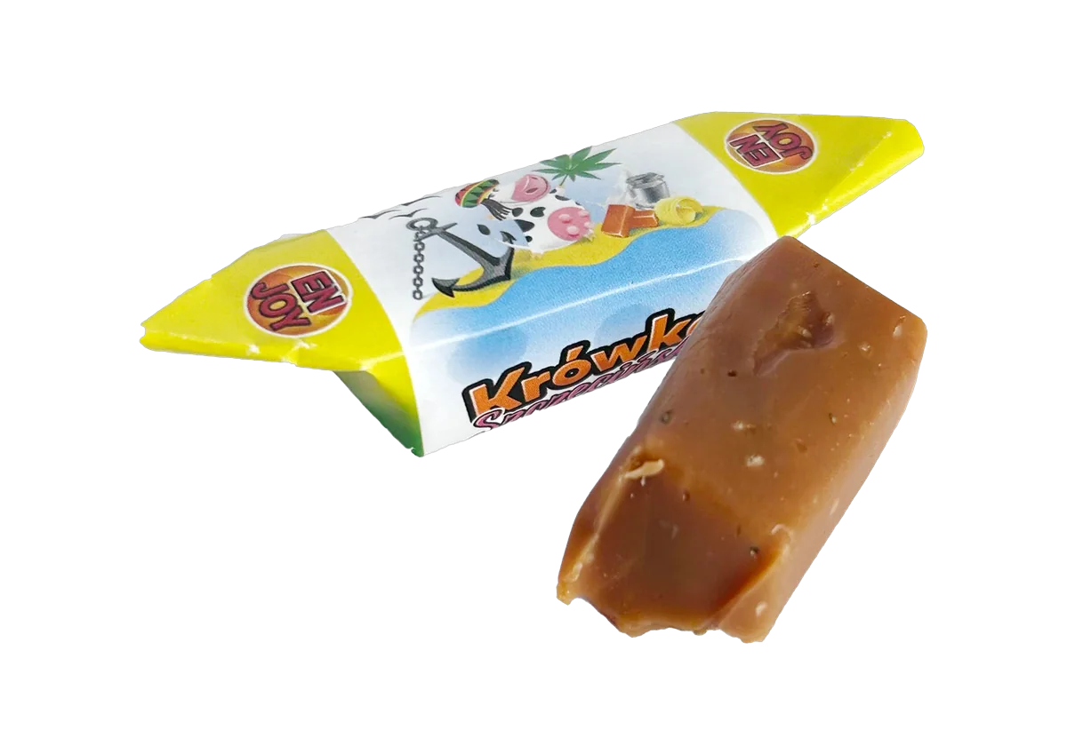Krówka Szczecińska Jamajka w żółto-niebieskim papierku, obok odwinięta kostka krówki z nasionami konopi